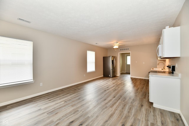 2026 Spruce St, Indianapolis, IN 46203 - unfurnished living room featuring light wood-type flooring, baseboards, a ceiling fan, a sink, and a textured ceiling