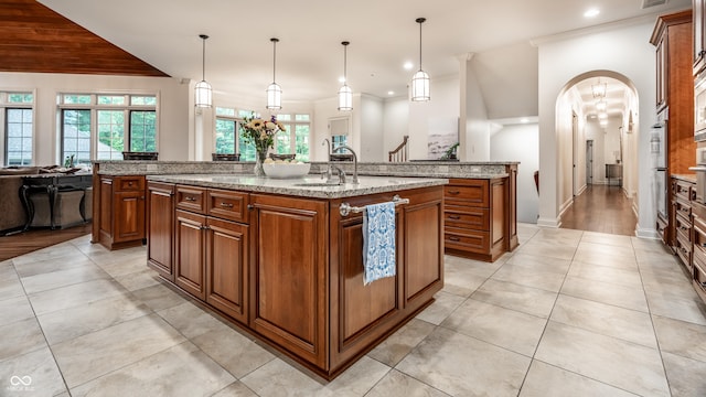 13346 W Sherbern Dr, Carmel, IN 46032 - kitchen featuring an island with sink, light tile patterned floors, brown cabinetry, recessed lighting, and light stone countertops
