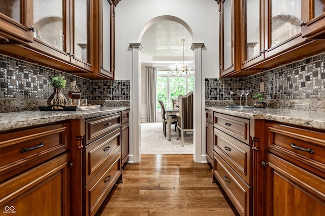 13346 W Sherbern Dr, Carmel, IN 46032 - kitchen with a chandelier, wood finished floors, tasteful backsplash, light stone counters, and crown molding