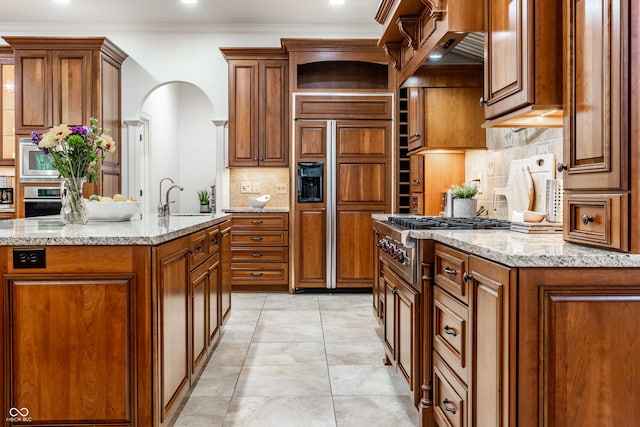 13346 W Sherbern Dr, Carmel, IN 46032 - kitchen featuring stainless steel appliances, brown cabinetry, tasteful backsplash, open shelves, and light stone counters