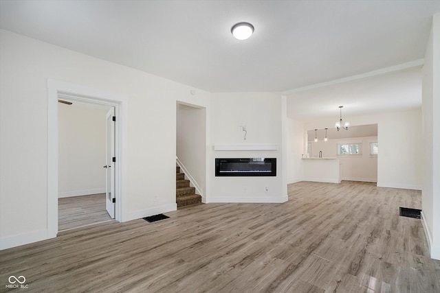 1038 W 33rd St, Indianapolis, IN 46208 - unfurnished living room with light wood-type flooring, a glass covered fireplace, a chandelier, and stairway
