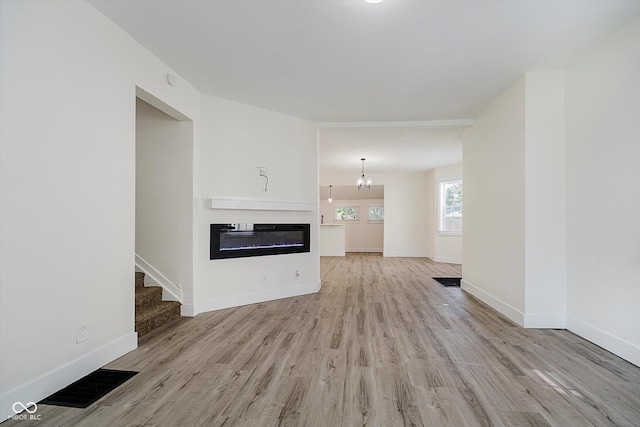1038 W 33rd St, Indianapolis, IN 46208 - unfurnished living room with light wood finished floors, a glass covered fireplace, stairway, and a chandelier