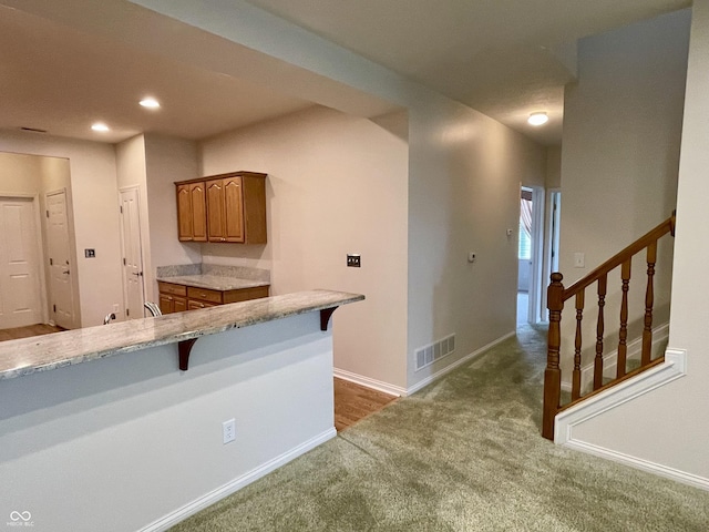 125 Bridgemor Ln, Mooresville, IN 46158 - kitchen featuring dark colored carpet, brown cabinetry, a breakfast bar area, light stone countertops, and baseboards