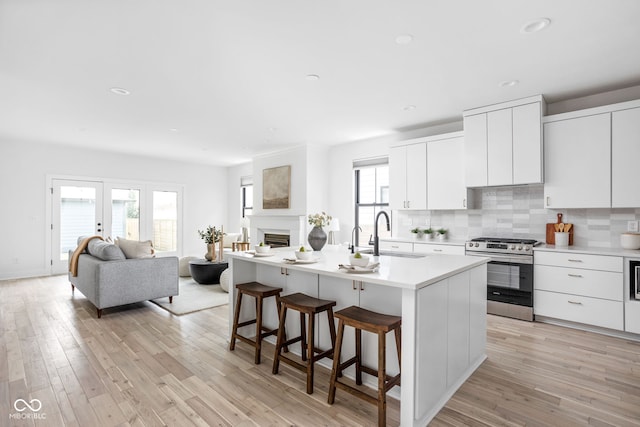 1717 Carrollton Ave, Indianapolis, IN 46202 - kitchen featuring stainless steel gas range oven, a kitchen breakfast bar, light countertops, decorative backsplash, and light wood-type flooring