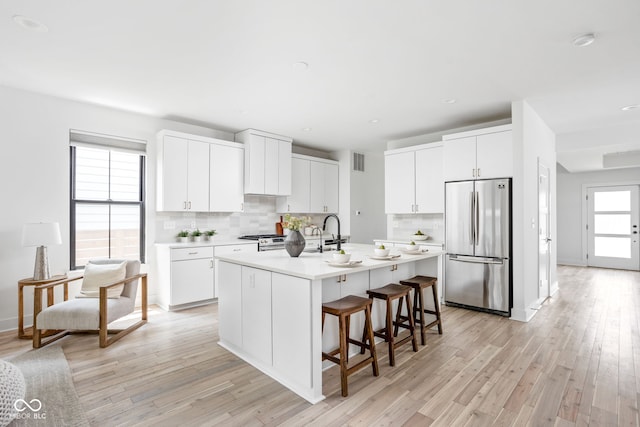 1717 Carrollton Ave, Indianapolis, IN 46202 - kitchen featuring appliances with stainless steel finishes, backsplash, light countertops, a kitchen island with sink, and a breakfast bar area