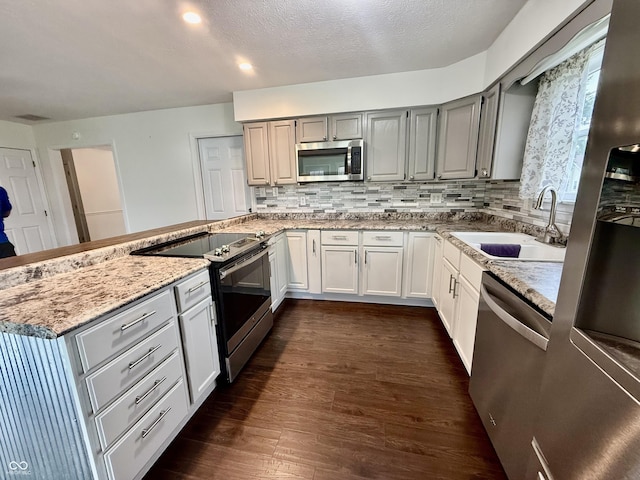 1002 Meadow Ln, Greencastle, IN 46135 - kitchen featuring appliances with stainless steel finishes, a sink, a peninsula, dark wood-style floors, and light stone countertops