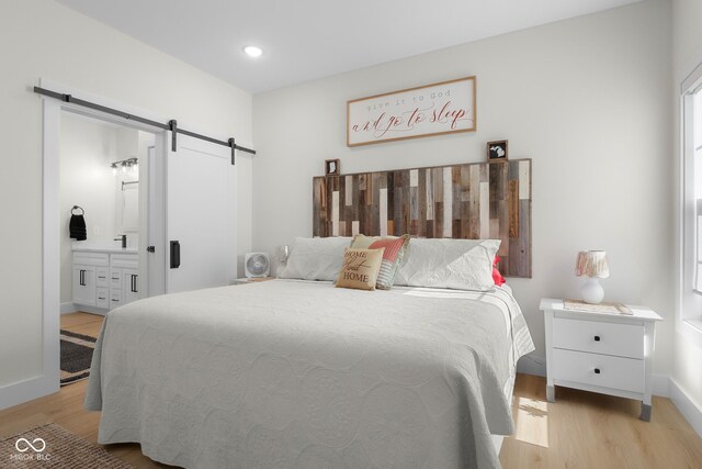 3365 Riverside Dr, Columbus, IN 47203 - bedroom featuring a barn door, light wood finished floors, baseboards, ensuite bath, and recessed lighting