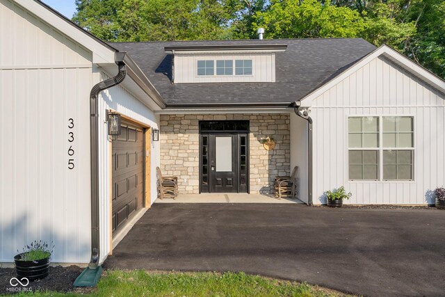 3365 Riverside Dr, Columbus, IN 47203 - entrance to property featuring stone siding, a garage, asphalt driveway, roof with shingles, and board and batten siding