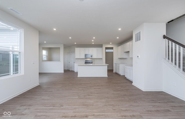 7151 Firestone Rd, Whitestown, IN 46052 - kitchen with stainless steel microwave, light wood finished floors, white cabinets, open floor plan, and recessed lighting