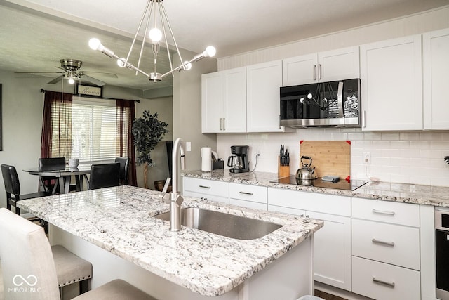 6180 Winnpeny Ln, Indianapolis, IN 46220 - kitchen featuring stainless steel microwave, black electric stovetop, a sink, and tasteful backsplash