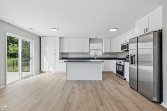 9949 Nightsong Ln, Avon, IN 46123 - kitchen with appliances with stainless steel finishes, dark countertops, white cabinetry, light wood finished floors, and a sink