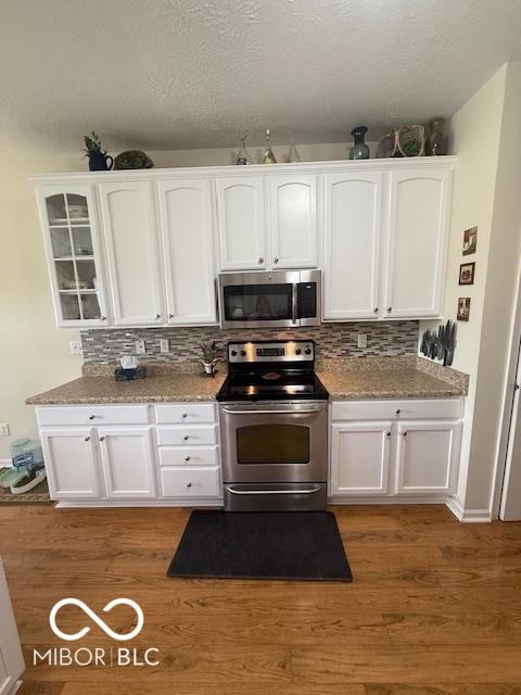 5304 Appleseed Way, Indianapolis, IN 46217 - kitchen with appliances with stainless steel finishes, white cabinets, backsplash, glass insert cabinets, and light wood-style flooring