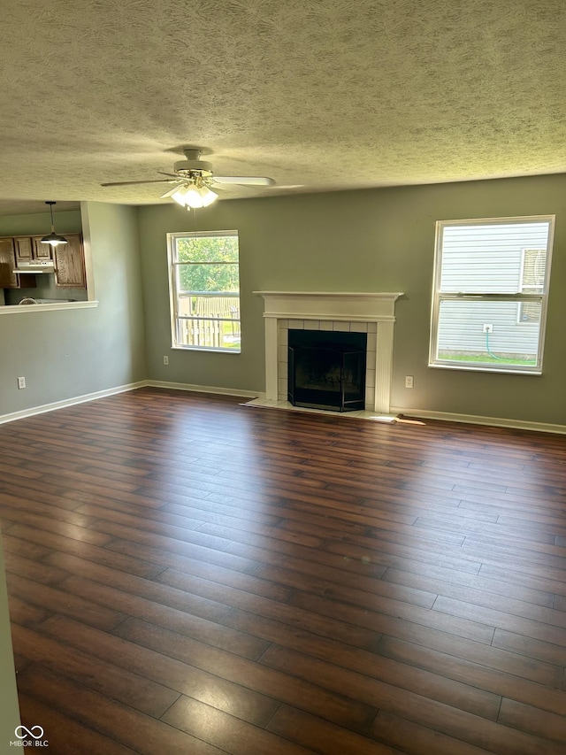 12307 Chiseled Stone Dr, Fishers, IN 46037 - unfurnished living room featuring a textured ceiling, ceiling fan, a tiled fireplace, dark wood finished floors, and baseboards