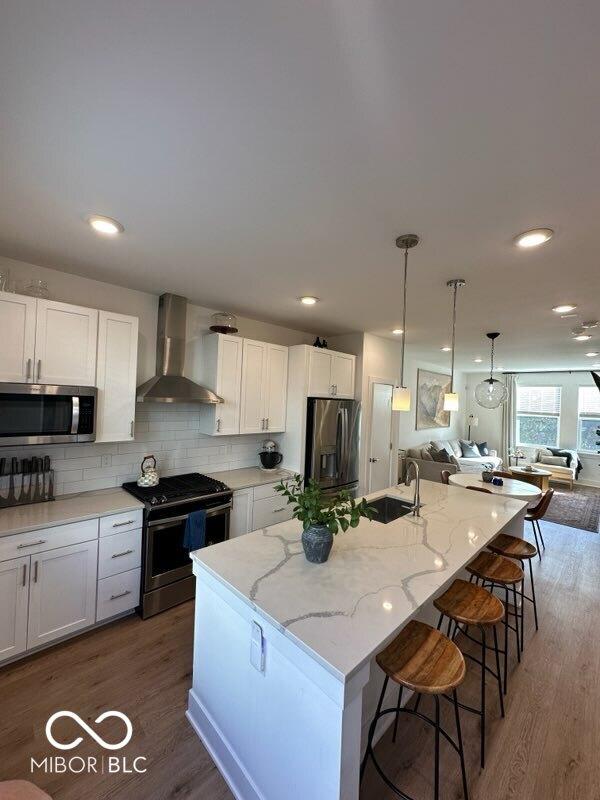 751 Switchyard Pl, Indianapolis, IN 46202 - kitchen featuring wall chimney exhaust hood, appliances with stainless steel finishes, a sink, white cabinetry, and light stone counters