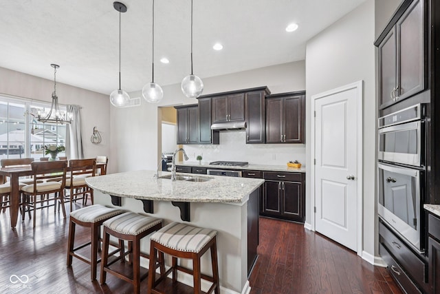 10806 Solis Cir, Fishers, IN 46038 - kitchen with under cabinet range hood, stainless steel appliances, decorative backsplash, light stone countertops, and a center island with sink