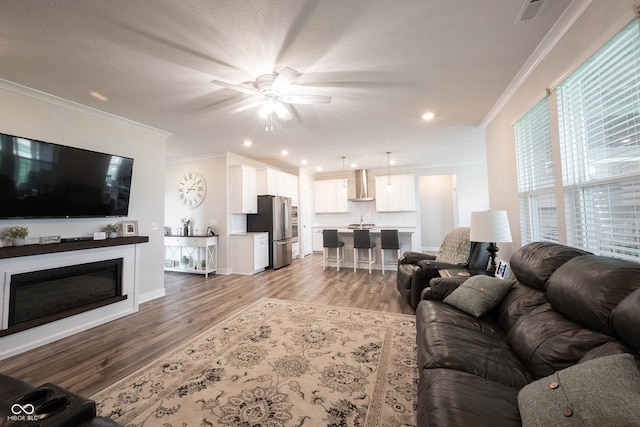 9671 Holborn Ave, Mccordsville, IN 46055 - living area with ornamental molding, ceiling fan, light wood-type flooring, a glass covered fireplace, and recessed lighting