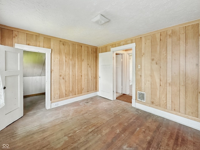 4709 E New York St, Indianapolis, IN 46201 - unfurnished bedroom featuring a textured ceiling, wood walls, wood finished floors, and baseboards