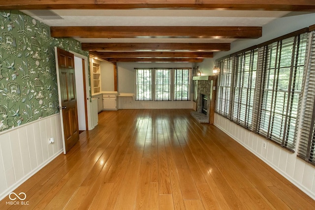 5530 Shawnee Trail S Drive, Indianapolis, IN 46220 - unfurnished living room featuring wallpapered walls, wainscoting, a stone fireplace, light wood finished floors, and beam ceiling