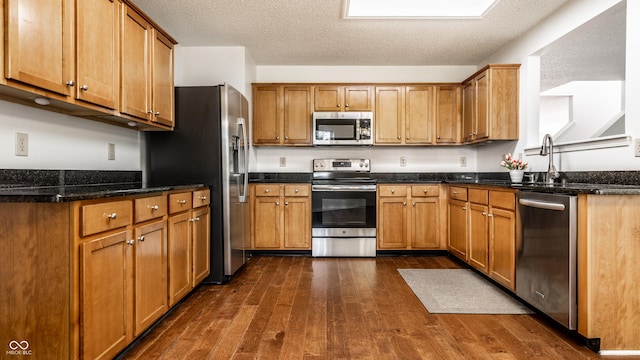 10216 Hatherley Way, Fishers, IN 46037 - kitchen featuring stainless steel appliances, dark wood-style floors, a textured ceiling, brown cabinetry, and dark stone countertops