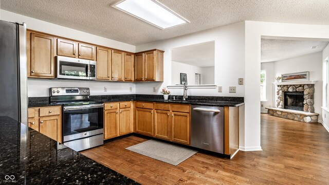10216 Hatherley Way, Fishers, IN 46037 - kitchen with stainless steel appliances, wood finished floors, a textured ceiling, a stone fireplace, and dark stone countertops