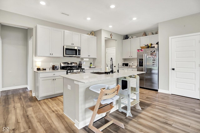 741 Scarsdale Ln, Danville, IN 46122 - kitchen featuring appliances with stainless steel finishes, light wood finished floors, a center island with sink, white cabinetry, and recessed lighting
