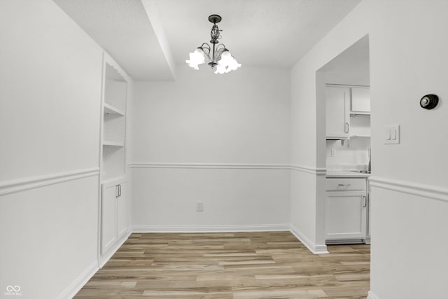 2642 Country Estates Dr, Indianapolis, IN 46227 - unfurnished dining area with a chandelier, light wood-type flooring, baseboards, a sink, and a textured ceiling