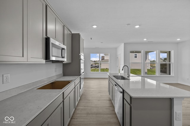 12490 Morning Ridge Way, Noblesville, IN 46060 - kitchen featuring gray cabinets, light wood-type flooring, a kitchen island with sink, appliances with stainless steel finishes, and light stone counters