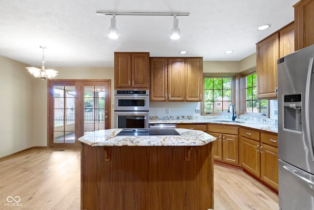 5037 Surrey Ln, Carmel, IN 46033 - kitchen with appliances with stainless steel finishes, light wood-style flooring, brown cabinetry, a kitchen island, and light stone counters