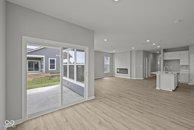 12500 Morning Ridge Way, Noblesville, IN 46060 - unfurnished living room with a glass covered fireplace, recessed lighting, light wood finished floors, baseboards, and a sink