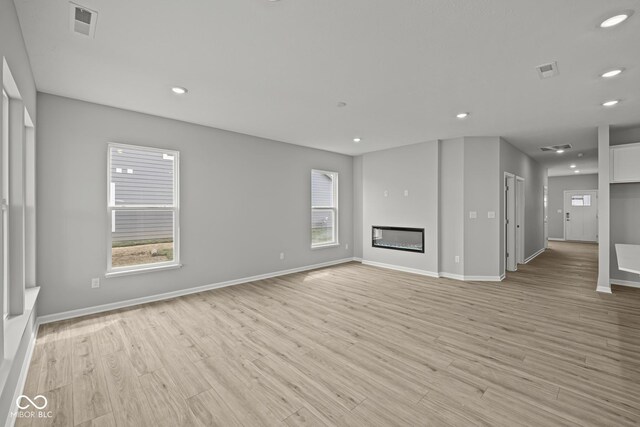 12500 Morning Ridge Way, Noblesville, IN 46060 - unfurnished living room with light wood-style flooring, baseboards, recessed lighting, and a glass covered fireplace