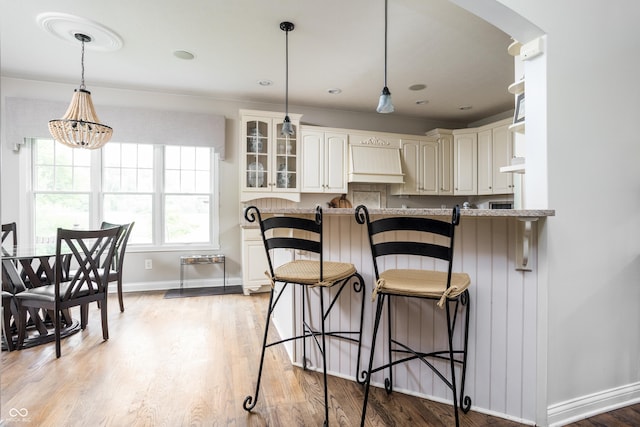 47 Torrey Pine Dr, Brownsburg, IN 46112 - kitchen with custom exhaust hood, glass insert cabinets, pendant lighting, a breakfast bar area, and light wood finished floors
