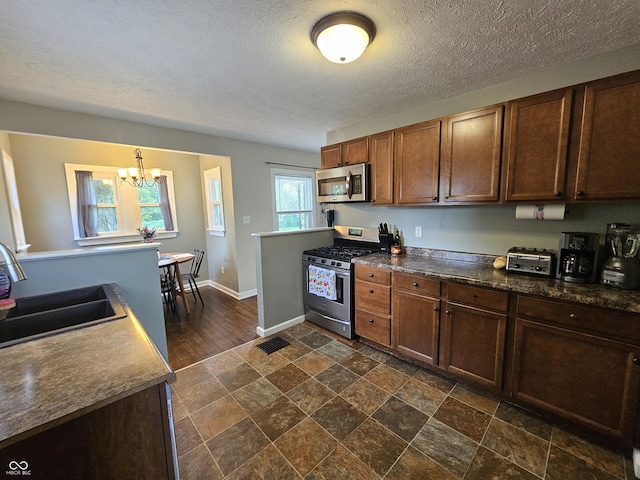 1510 Chester St, Anderson, IN 46012 - kitchen featuring appliances with stainless steel finishes, a chandelier, dark stone finish floors, dark countertops, and a textured ceiling