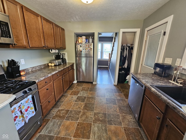 1510 Chester St, Anderson, IN 46012 - kitchen with appliances with stainless steel finishes, dark countertops, brown cabinets, a textured ceiling, and dark stone finish flooring