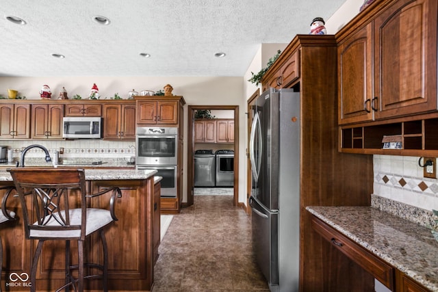 5194 Orahood Ct, Plainfield, IN 46168 - kitchen with stainless steel appliances, washing machine and dryer, tasteful backsplash, a textured ceiling, and light stone counters