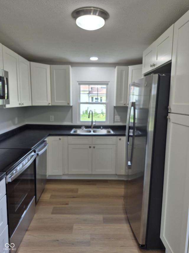 1501 California St, Columbus, IN 47201 - kitchen featuring appliances with stainless steel finishes, white cabinetry, dark countertops, light wood finished floors, and a textured ceiling