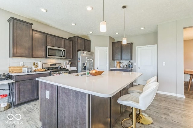 1758 Pelham Dr, Greenwood, IN 46143 - kitchen with appliances with stainless steel finishes, light wood-style floors, a center island with sink, dark brown cabinetry, and recessed lighting