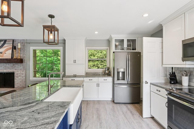 7029 Kingswood Cir, Indianapolis, IN 46256 - kitchen featuring appliances with stainless steel finishes, a fireplace, white cabinetry, light wood-style floors, and light stone counters