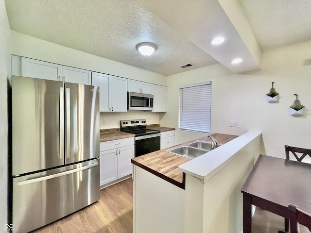 7392 S Meridian St, Indianapolis, IN 46217 - kitchen with stainless steel appliances, light wood-type flooring, a textured ceiling, a peninsula, and butcher block countertops