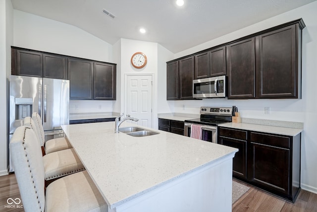 6608 W Shoreline Ct, Greenfield, IN 46140 - kitchen featuring appliances with stainless steel finishes, light stone countertops, lofted ceiling, a kitchen island with sink, and light wood-style flooring
