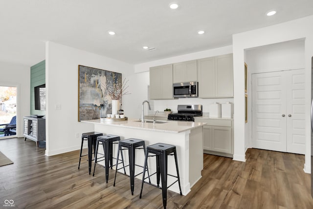 703 Penrose Pl, Danville, IN 46122 - kitchen featuring stainless steel microwave, range with gas stovetop, dark wood finished floors, an island with sink, and a kitchen breakfast bar