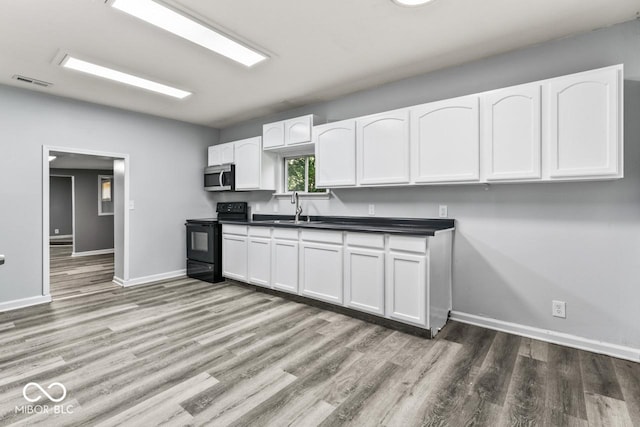 3529 Hunt St, Plainfield, IN 46168 - kitchen with black range with electric cooktop, stainless steel microwave, wood finished floors, and white cabinetry