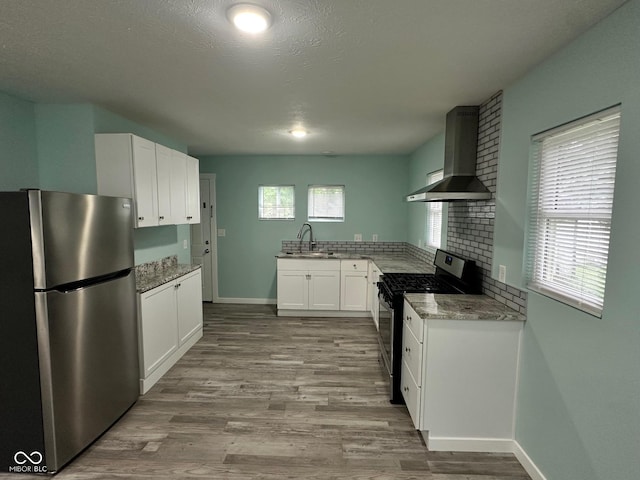 4715 Normal Ave, Indianapolis, IN 46226 - kitchen with freestanding refrigerator, wall chimney exhaust hood, gas range oven, white cabinetry, and light wood-type flooring