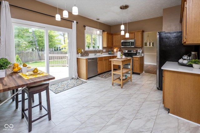 14492 Cotswold Ln, Carmel, IN 46033 - kitchen with stainless steel appliances, brown cabinetry, light countertops, and pendant lighting