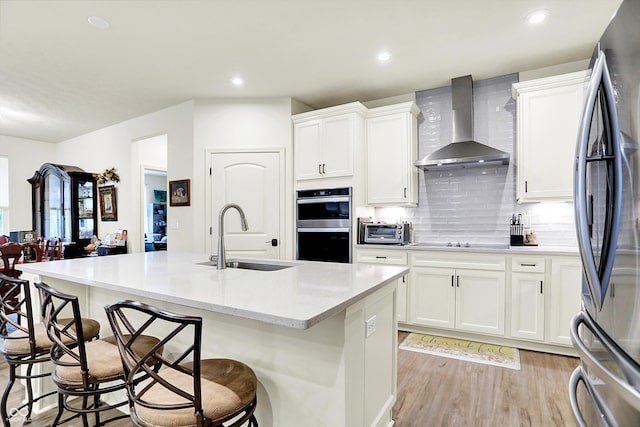 2612 Ruffian Dr, Westfield, IN 46074 - kitchen with wall chimney exhaust hood, appliances with stainless steel finishes, a breakfast bar, light wood-style floors, and an island with sink