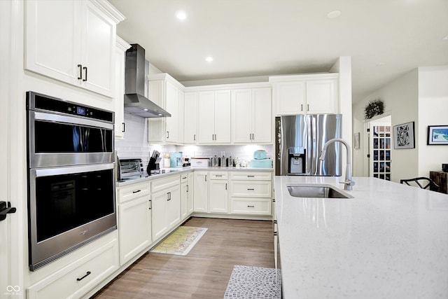 2612 Ruffian Dr, Westfield, IN 46074 - kitchen featuring wall chimney range hood, appliances with stainless steel finishes, light wood-style flooring, decorative backsplash, and light stone counters