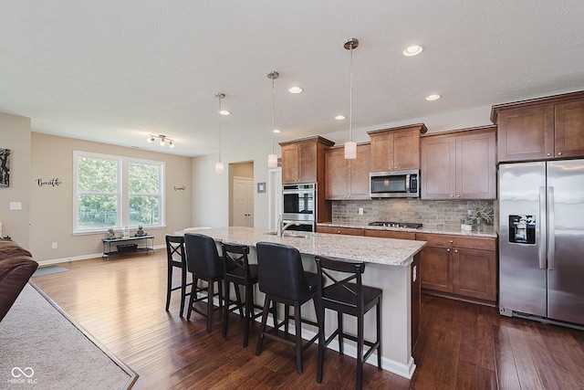 11840 Crossbill Ct, Noblesville, IN 46060 - kitchen with appliances with stainless steel finishes, dark wood-style flooring, tasteful backsplash, a breakfast bar area, and light stone countertops