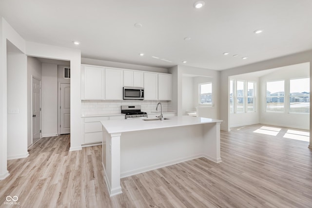 18955 Seaforth Way, Westfield, IN 46074 - kitchen featuring stainless steel appliances, light wood-style flooring, backsplash, a kitchen island with sink, and light countertops