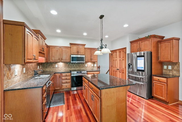5274 Brooks Bnd, Greenwood, IN 46143 - kitchen featuring appliances with stainless steel finishes, a kitchen island, light wood-style floors, tasteful backsplash, and dark stone countertops