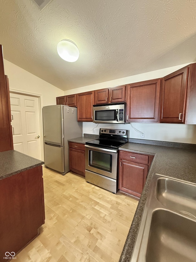 5019 Amber Creek Pl, Indianapolis, IN 46237 - kitchen with appliances with stainless steel finishes, dark countertops, light wood-type flooring, lofted ceiling, and a textured ceiling