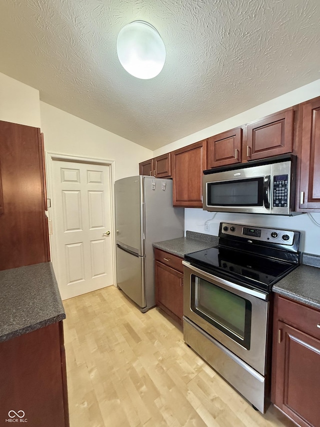 5019 Amber Creek Pl, Indianapolis, IN 46237 - kitchen with appliances with stainless steel finishes, dark countertops, vaulted ceiling, light wood finished floors, and a textured ceiling
